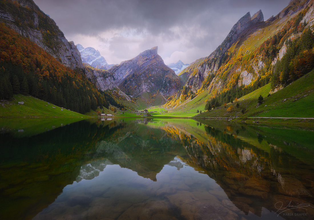Lake Seealpsee | A gorgeous lake surrounded by colorful trees in the Appenzell region of Switzerland, in October, before a rain storm.  Santis mountain is visible in the distance through the clouds.