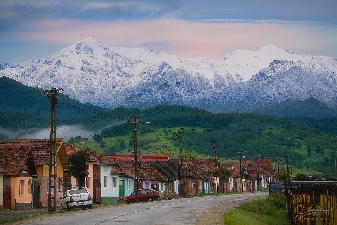 Rasnov, Romania | Typical houses along the road in Rasnov village, Brasov county, Romania, with snowy mountain peaks (Carpathians) in the background
